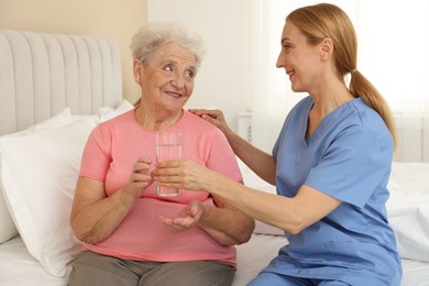 Photo of Healthcare worker giving glass of water to senior patient at home