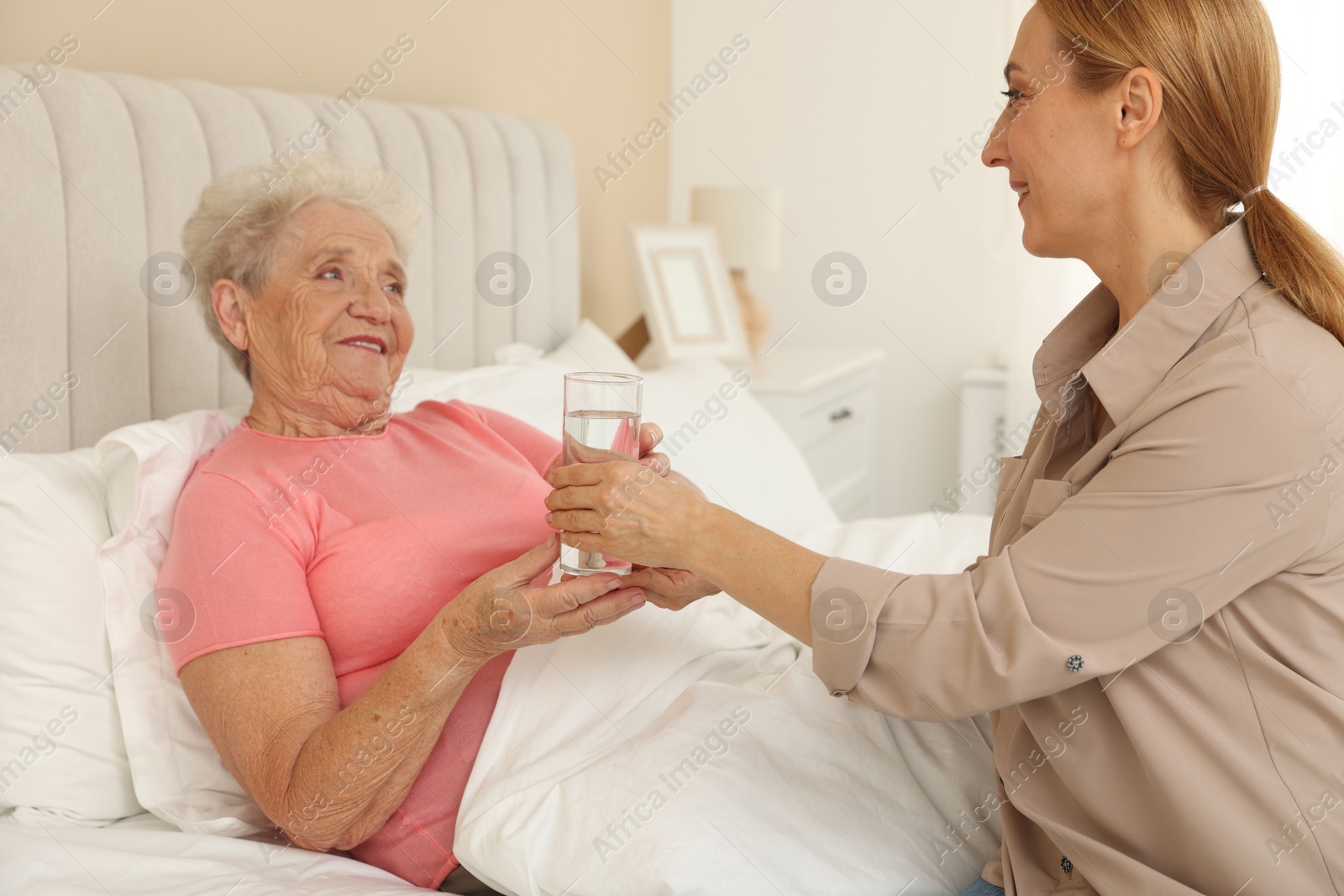 Photo of Caregiver giving glass of water to senior woman at home