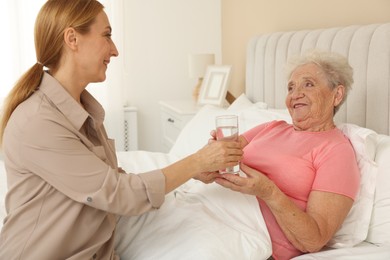 Photo of Caregiver giving glass of water to senior woman at home