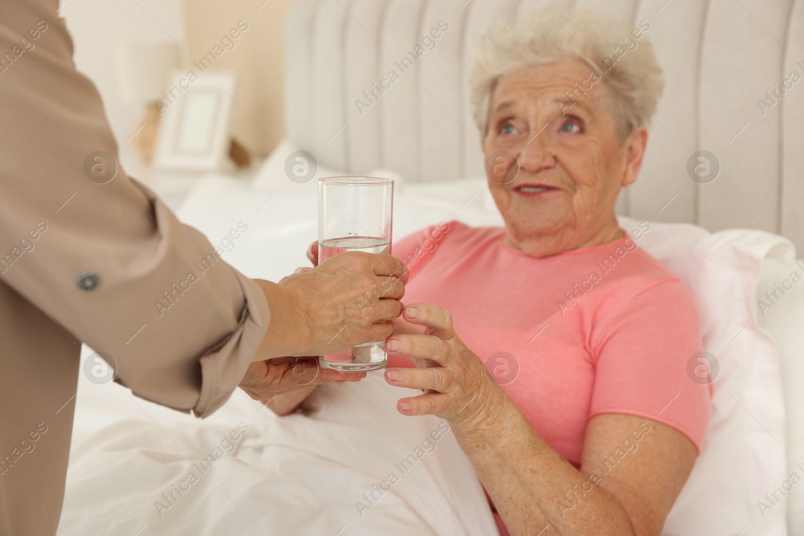 Photo of Caregiver giving glass of water to senior patient at home, selective focus