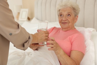 Caregiver giving glass of water to senior patient at home, selective focus