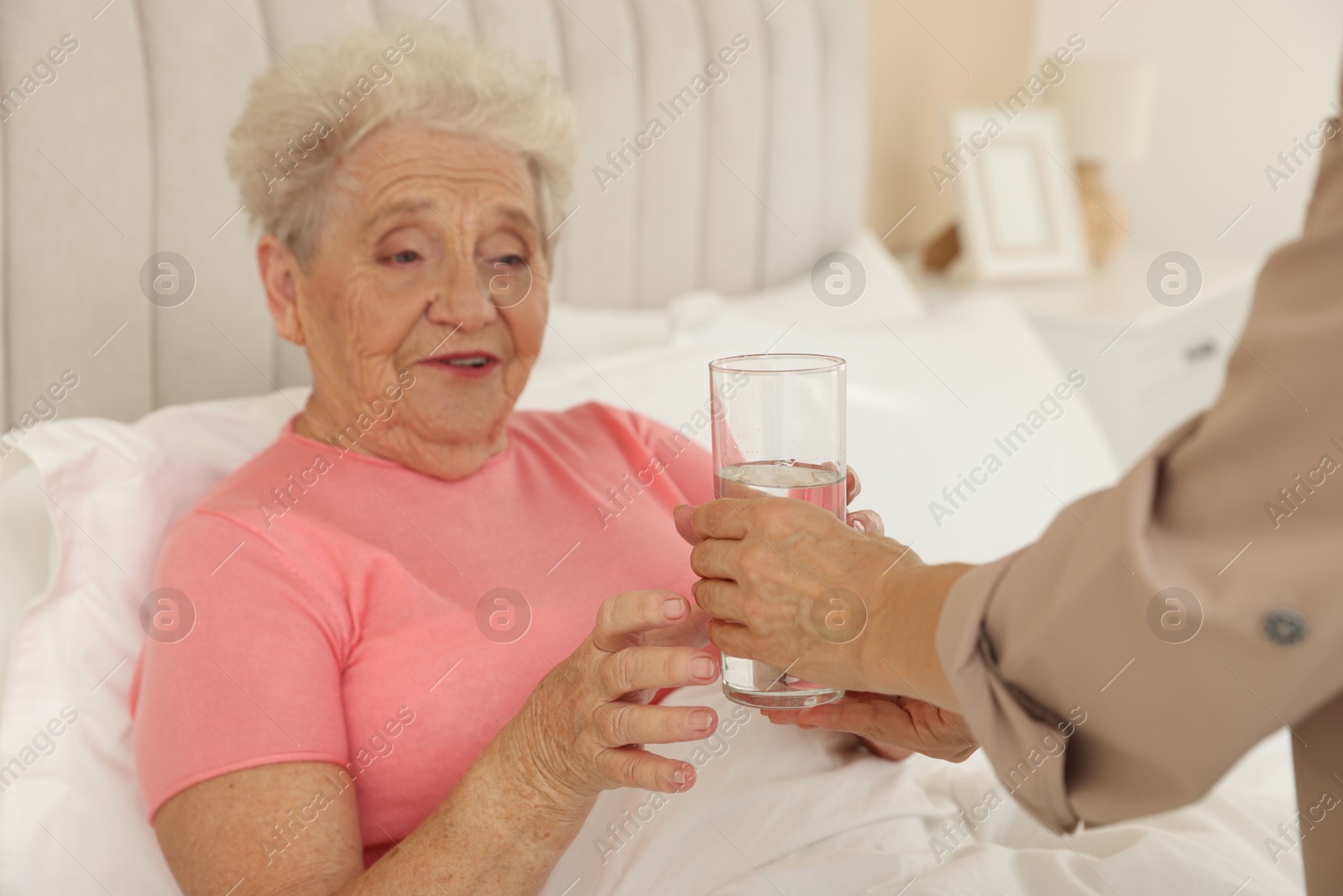 Photo of Caregiver giving glass of water to senior patient at home, selective focus