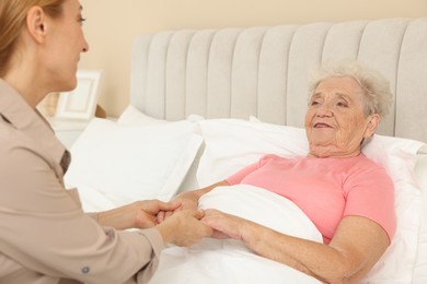 Photo of Caregiver supporting senior patient in bedroom at home