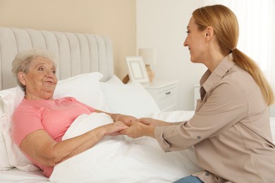 Photo of Caregiver supporting senior patient in bedroom at home