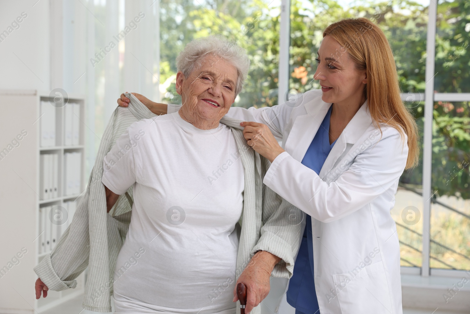 Photo of Healthcare worker helping senior patient to wear jacket in hospital