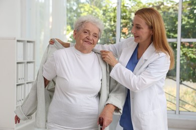 Healthcare worker helping senior patient to wear jacket in hospital