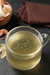 Photo of Hot delicious bouillon with dill in glass cup on black table