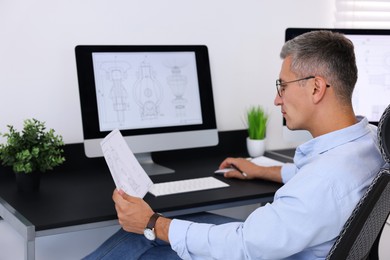 Architect checking engineering drawing at table in office