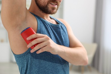 Smiling man applying solid deodorant at home, closeup