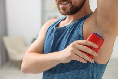 Photo of Smiling man applying solid deodorant at home, closeup