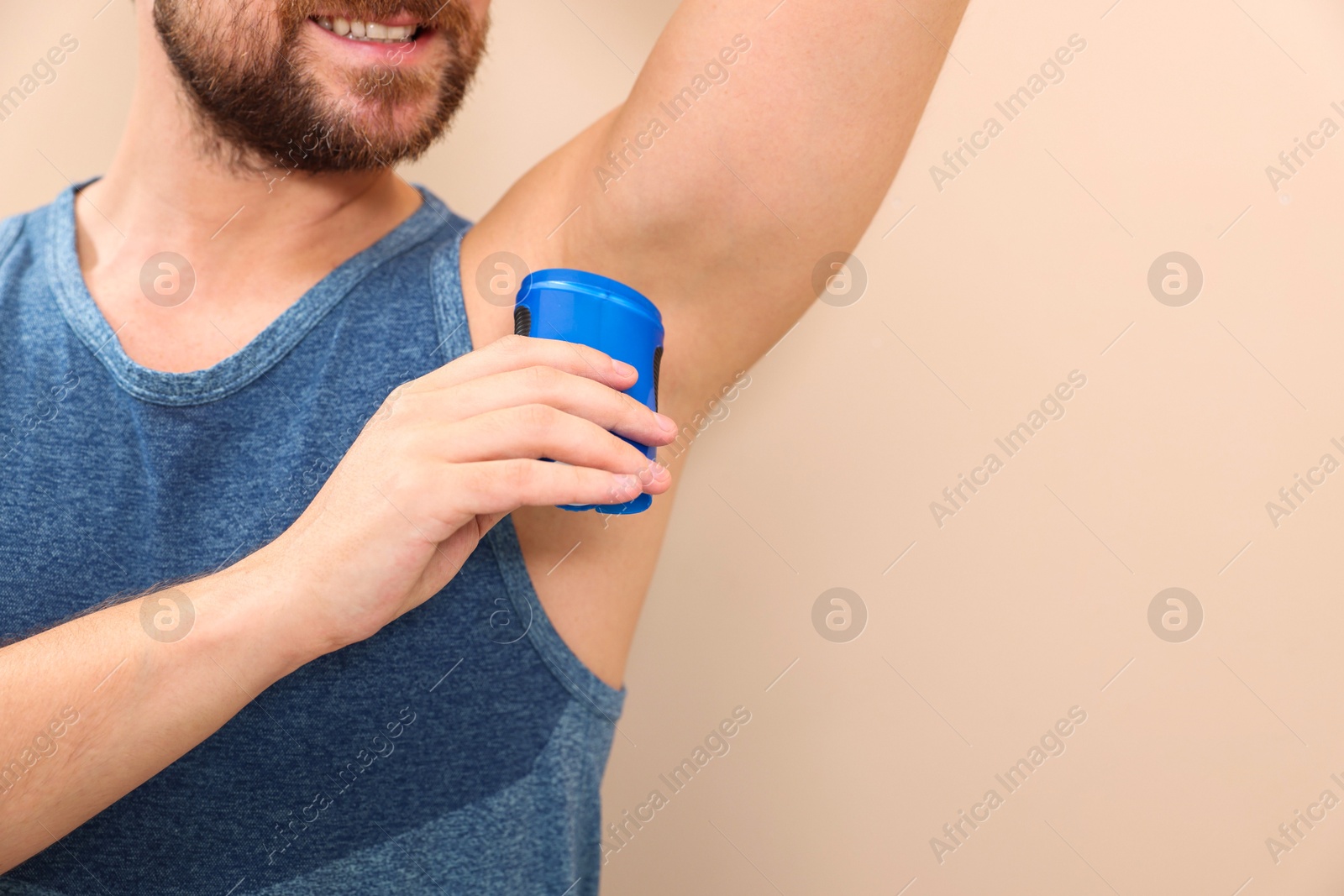 Photo of Smiling man applying solid deodorant on beige background, closeup. Space for text