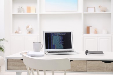 Photo of Programmer's workplace. Modern laptop with unfinished code, cup and notebooks on desk indoors