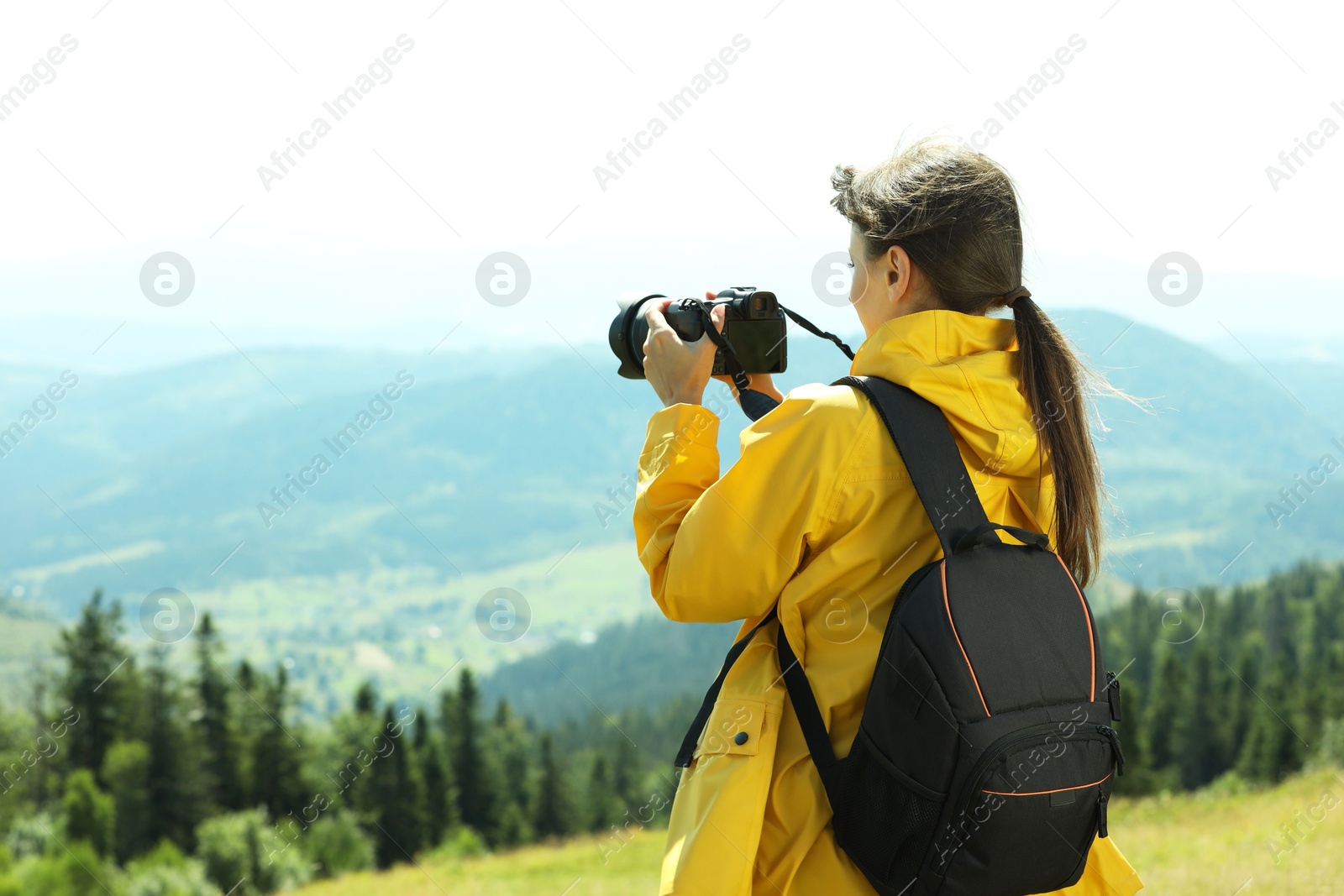 Photo of Photographer with backpack and camera taking picture of beautiful mountains, back view