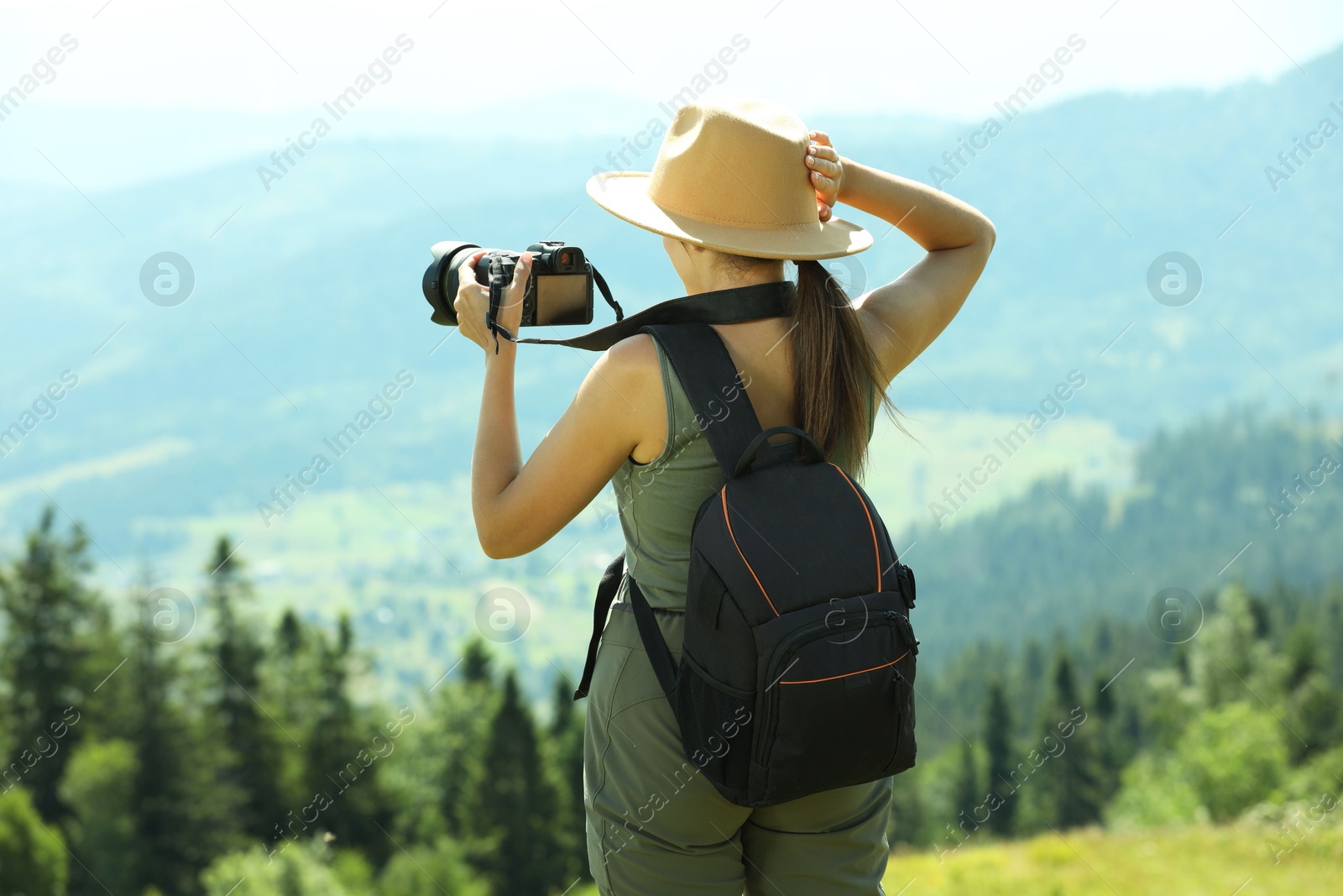 Photo of Photographer with backpack and camera taking picture of beautiful mountains, back view