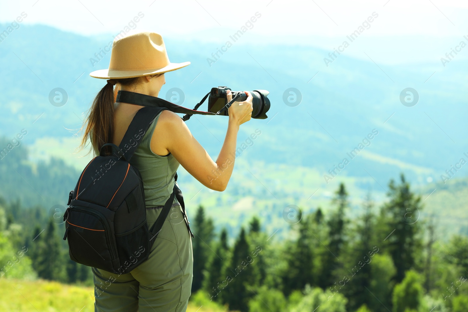 Photo of Photographer with backpack and camera taking picture of beautiful mountains, back view. Space for text