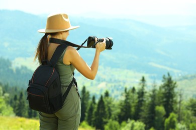 Photographer with backpack and camera taking picture of beautiful mountains, back view. Space for text