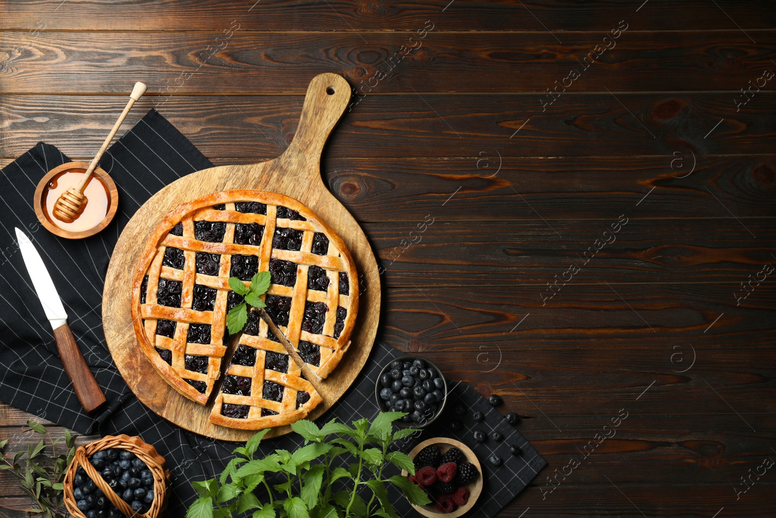 Photo of Tasty homemade pie with blueberries, fresh berries, mint, honey and knife on wooden table, flat lay. Space for text