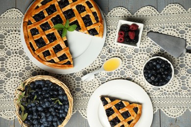 Photo of Tasty homemade pie with blueberries, fresh berries honey and cake server on gray wooden table, flat lay