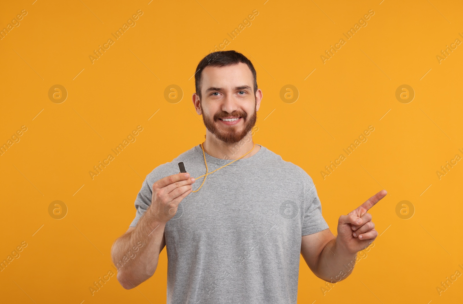 Photo of Happy young man with whistle on orange background