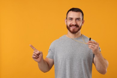 Happy young man with whistle on orange background, space for text