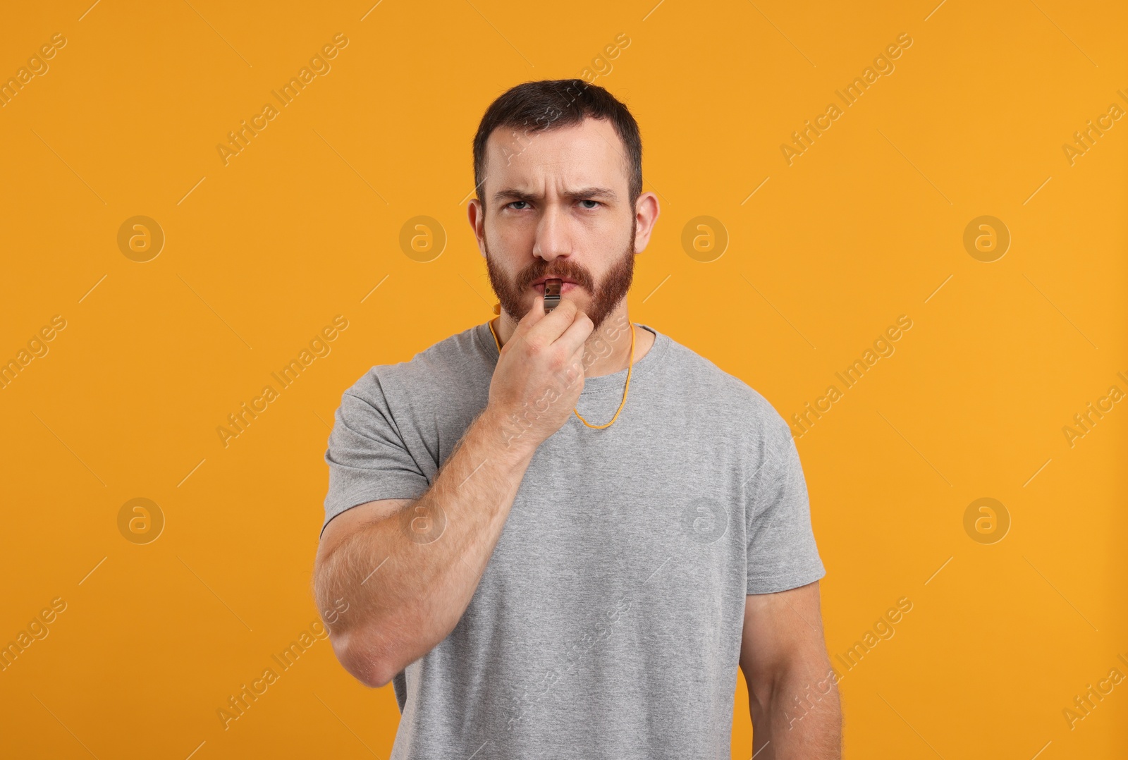 Photo of Young man blowing whistle on orange background