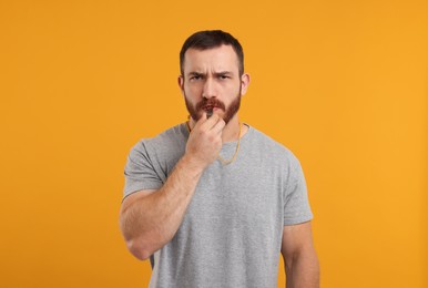 Young man blowing whistle on orange background