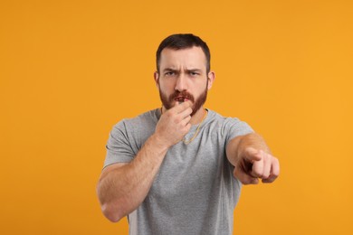 Young man blowing whistle on orange background