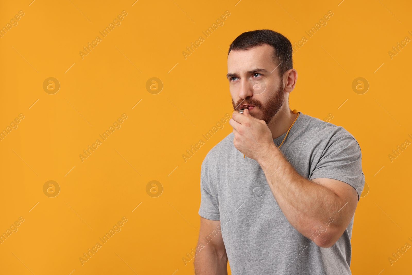 Photo of Young man blowing whistle on orange background, space for text