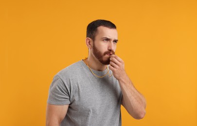 Young man blowing whistle on orange background