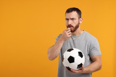 Photo of Young man with soccer ball blowing whistle on orange background, space for text