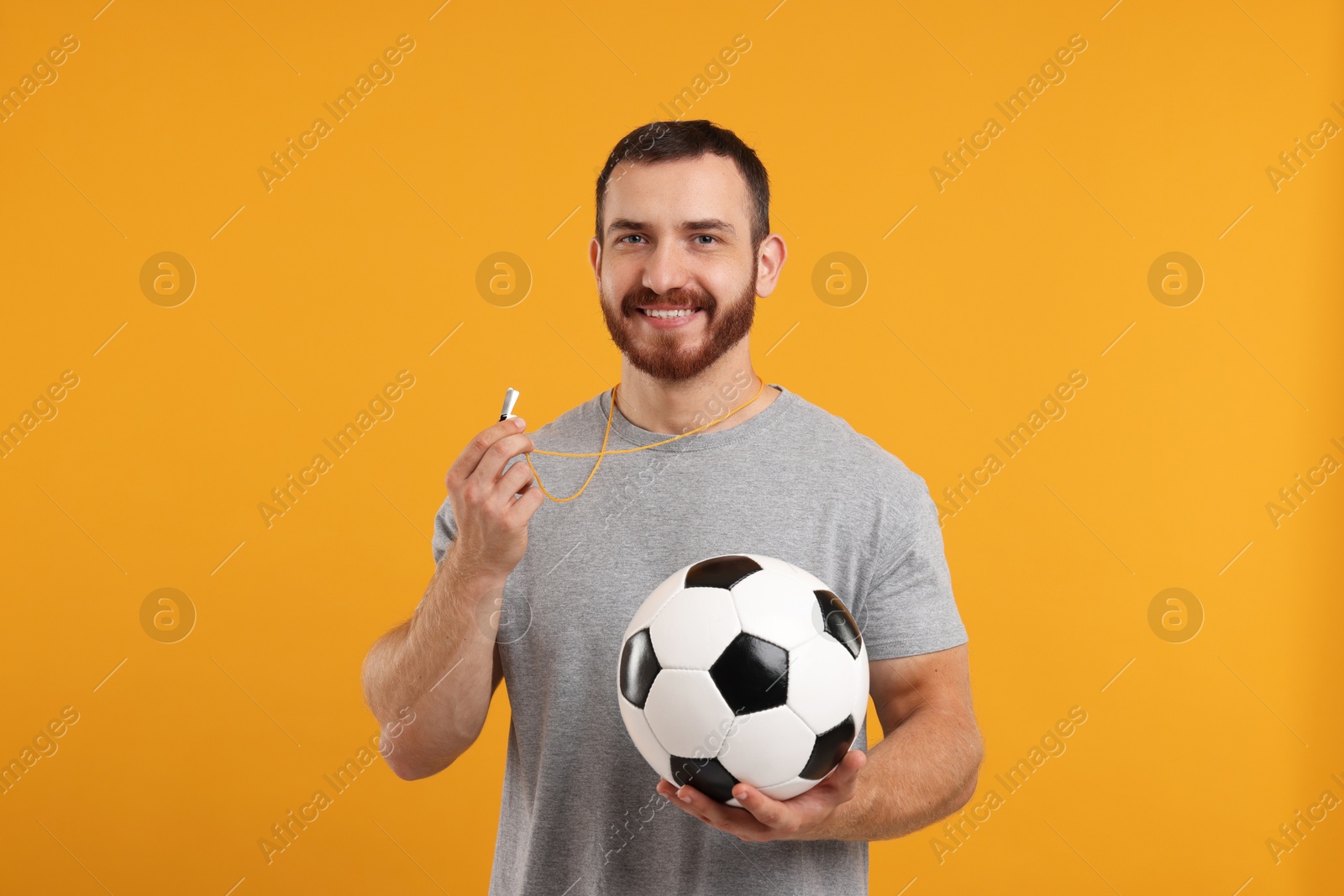 Photo of Happy young man with whistle and soccer ball on orange background