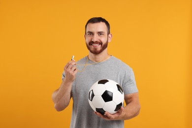 Photo of Happy young man with whistle and soccer ball on orange background