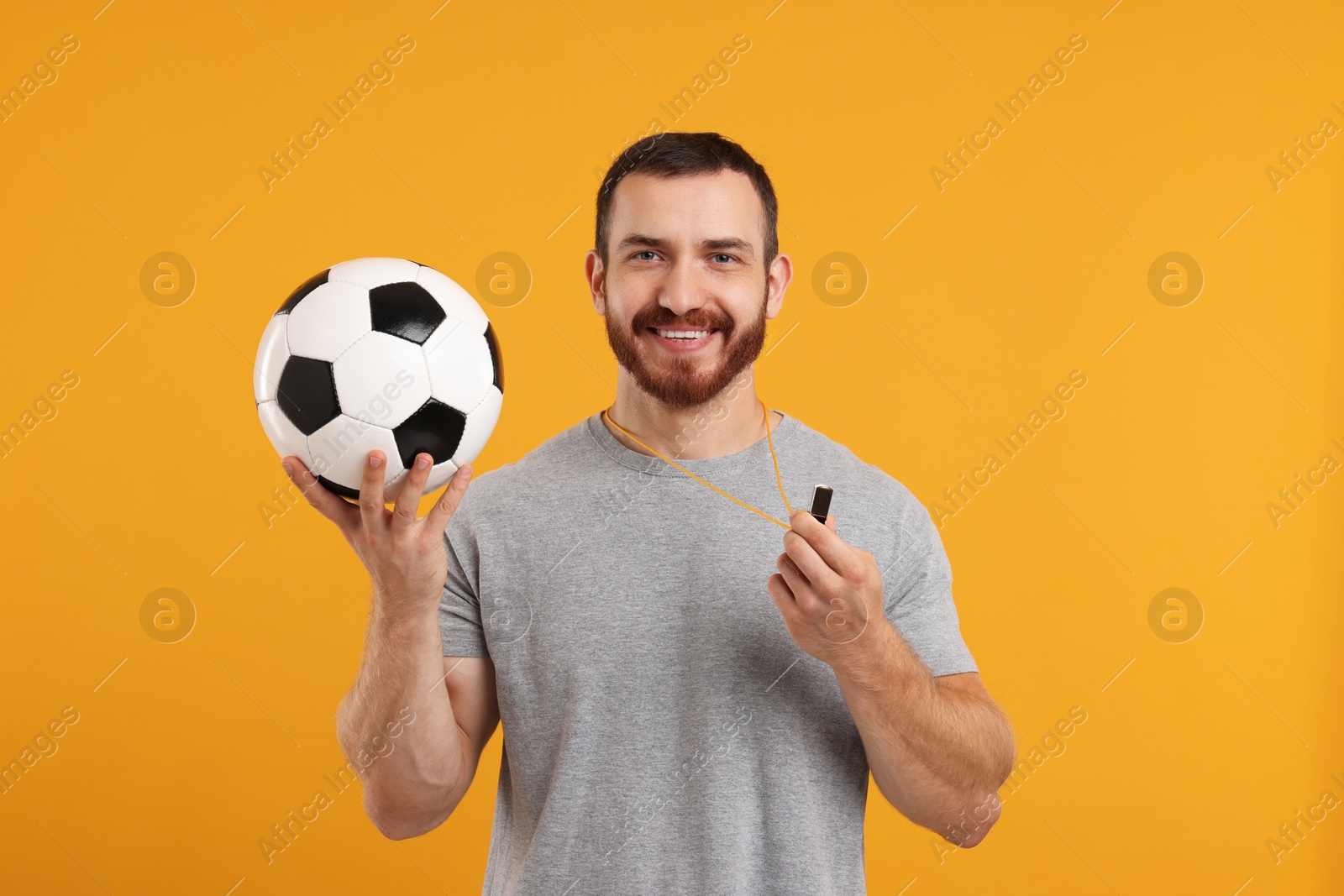 Photo of Happy young man with whistle and soccer ball on orange background