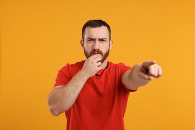 Young man blowing whistle on orange background