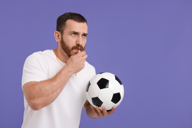 Photo of Young man with soccer ball blowing whistle on purple background, space for text