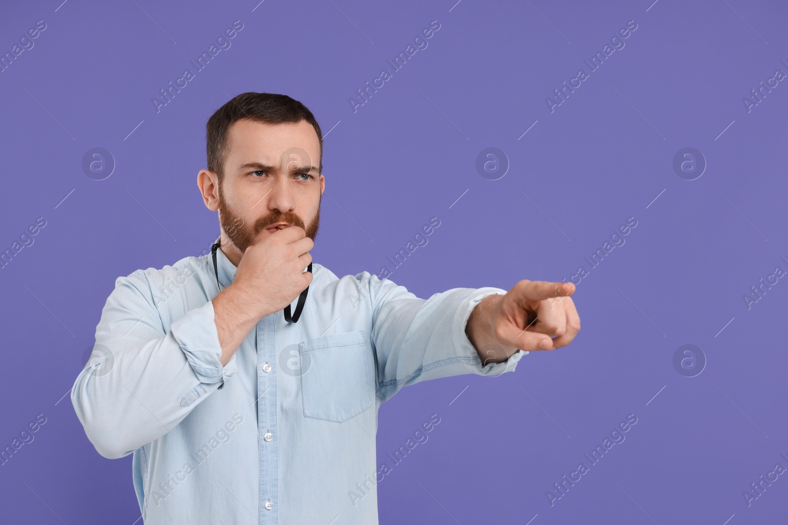 Photo of Young man blowing whistle on purple background, space for text