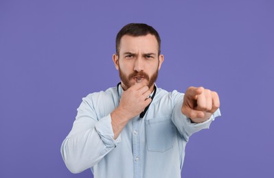 Photo of Young man blowing whistle on purple background