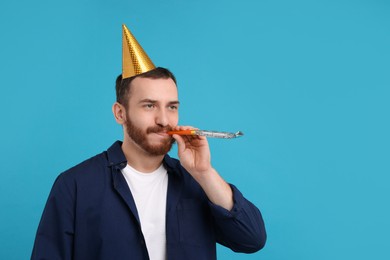 Man in party hat with blower on light blue background, space for text