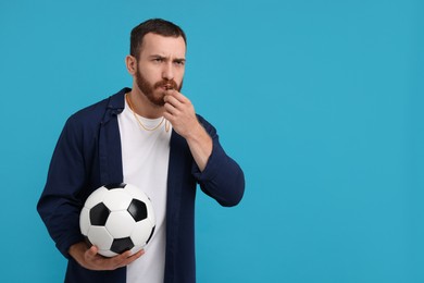 Photo of Young man with soccer ball blowing whistle on light blue background, space for text