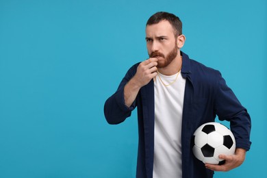 Photo of Young man with soccer ball blowing whistle on light blue background, space for text