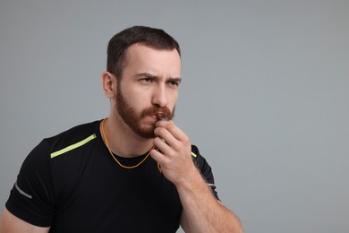 Young man blowing whistle on grey background, space for text