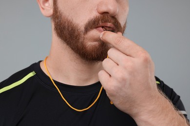 Photo of Man blowing whistle on grey background, closeup