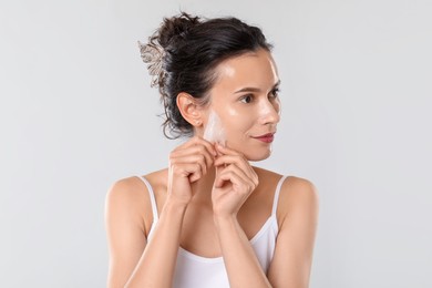 Photo of Beautiful woman peeling off face mask on light grey background