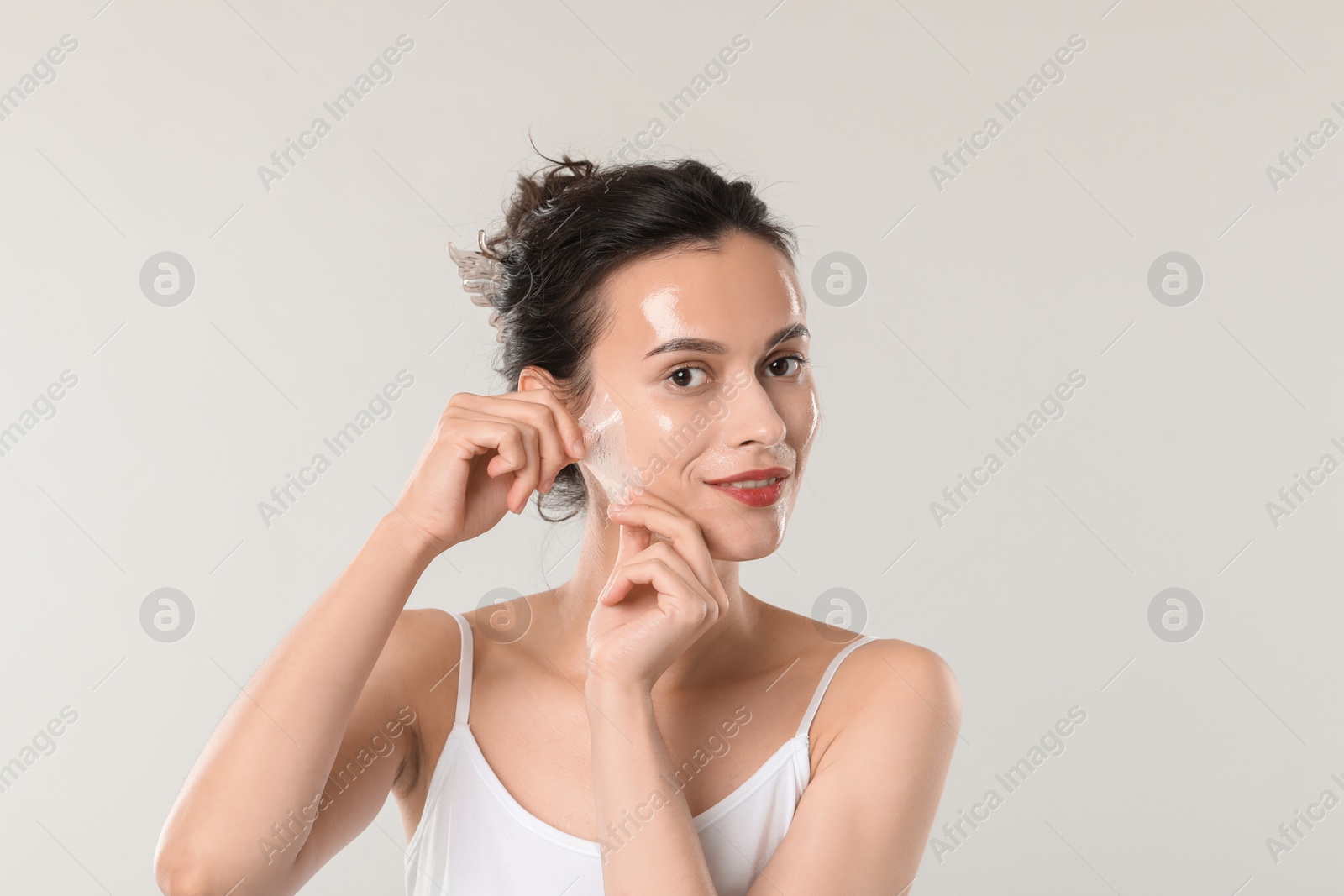 Photo of Smiling woman peeling off face mask on light grey background