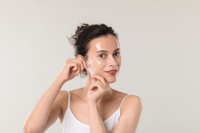 Photo of Smiling woman peeling off face mask on light grey background