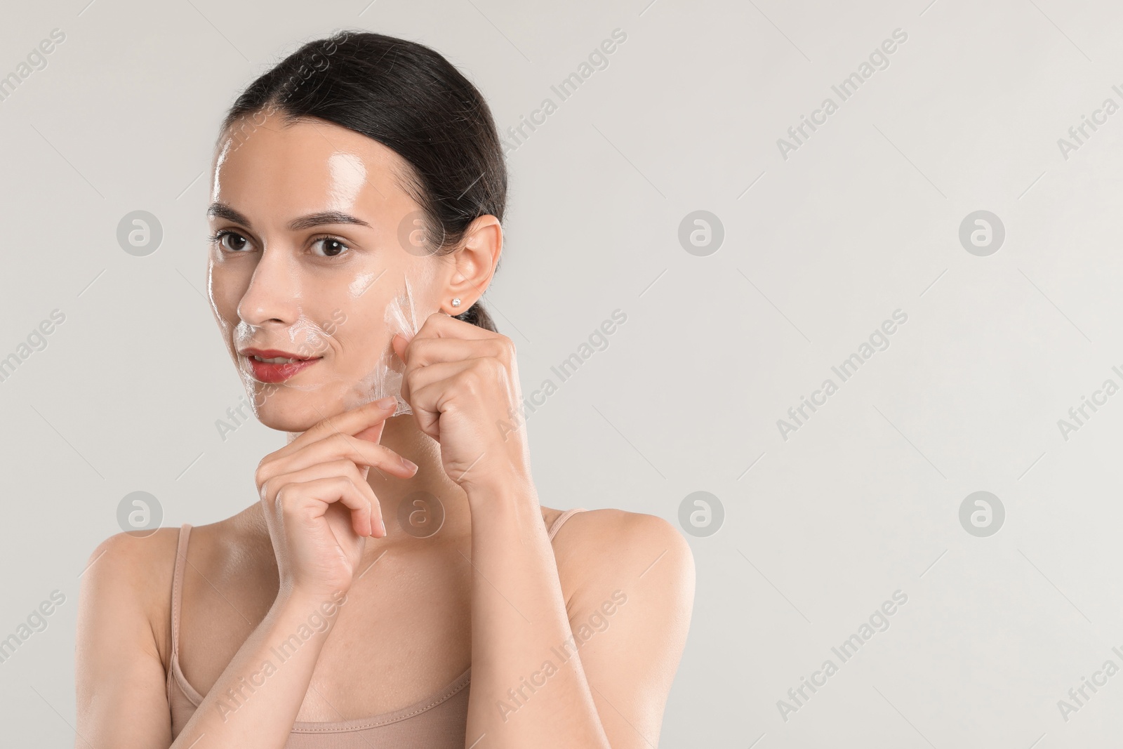 Photo of Smiling woman peeling off face mask on light grey background. Space for text