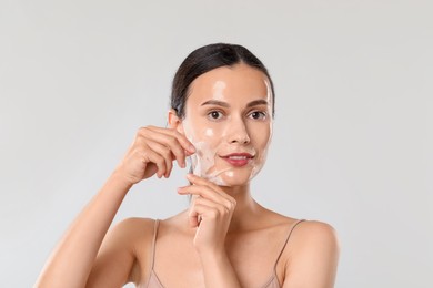 Photo of Smiling woman peeling off face mask on light grey background