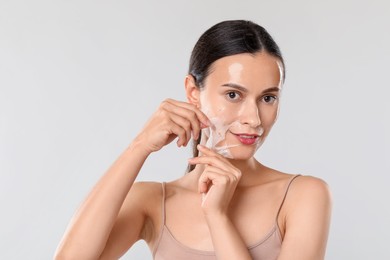 Photo of Beautiful woman peeling off face mask on light grey background