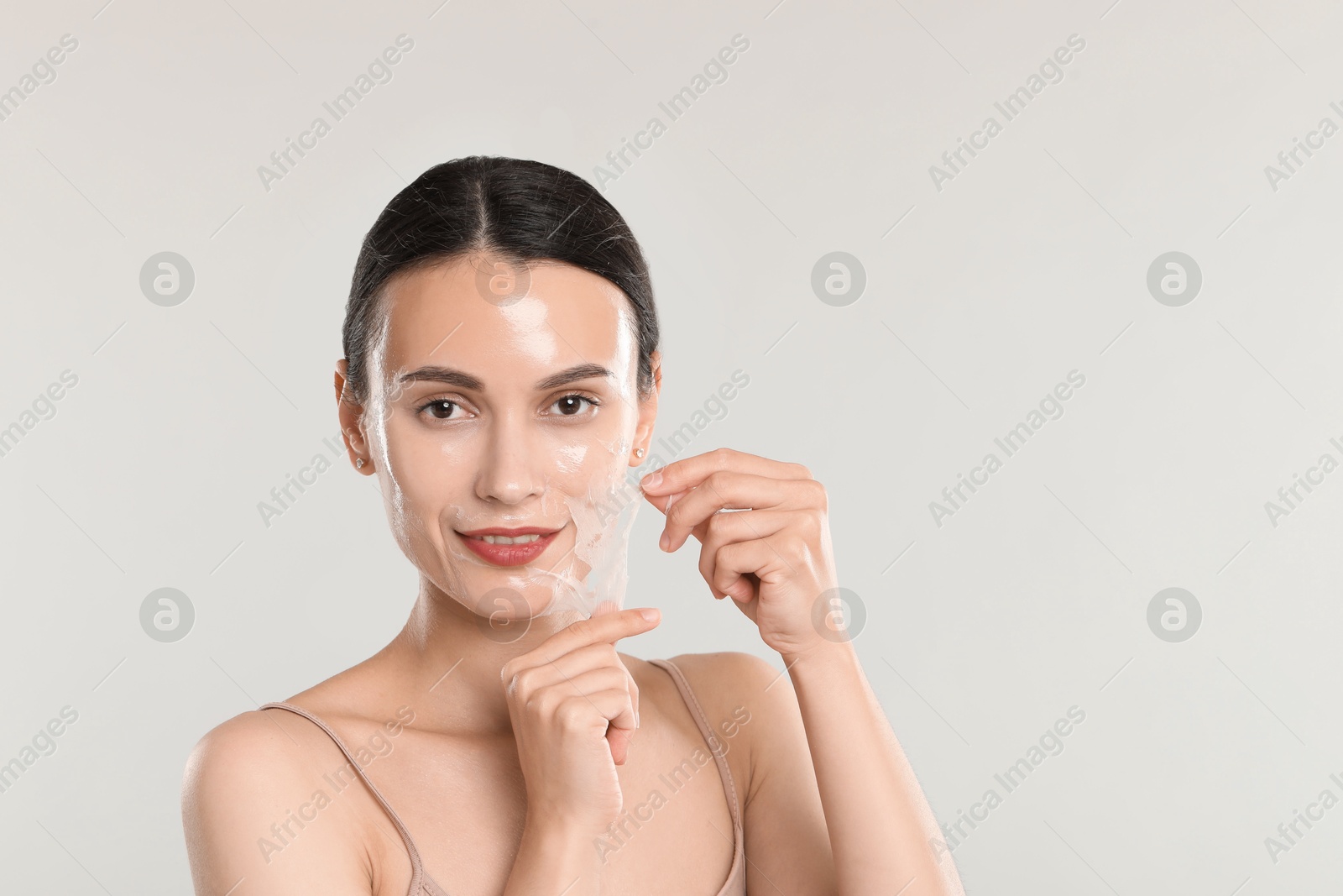 Photo of Smiling woman peeling off face mask on light grey background. Space for text