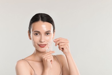 Smiling woman peeling off face mask on light grey background. Space for text